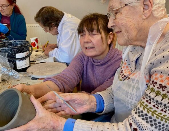 Two ladies sitting at a table doing pottery