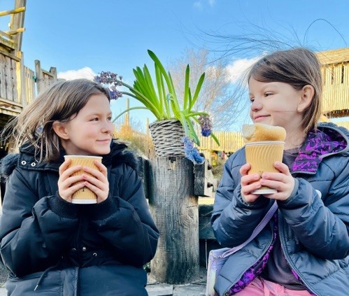 Two children drinking hot drinks outside