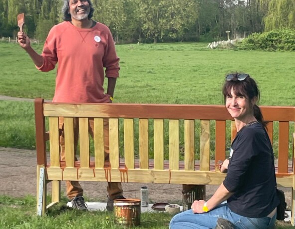 Man and a woman painting a park bench.