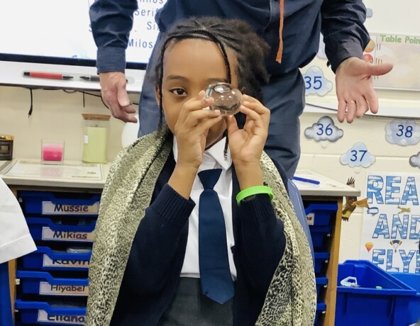 Young school girl looking through a looking glass